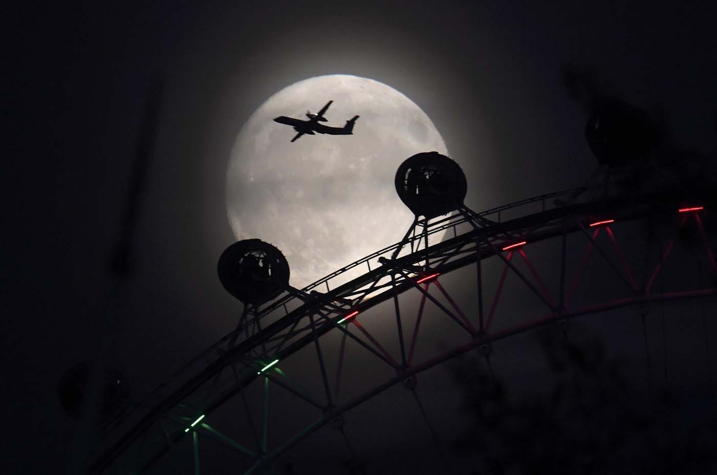 An aeroplane flies past the London Eye wheel, and moon, a day before the "supermoon" spectacle in London, Britain, November 13, 2016. REUTERS/Toby Melville