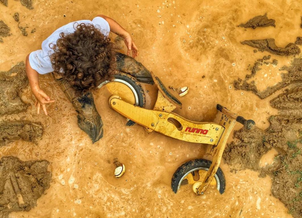 TERCER LUGAR, NIÑOS "Esta foto fue tomada en una zona rural de Río llamada Vargem Grande, donde Felipe, de 3 años y mi hijo mayor, le encanta explorar la pista de motocross con su moto de madera. La lluvia que no podía resistir saltar en ella.".