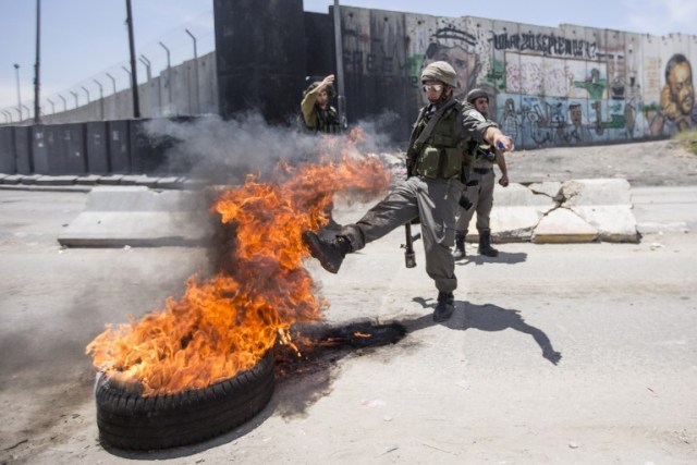 Un guardia fronterizo israelí patea un neumático ardiendo durante los enfrentamientos con jóvenes palestinos en el cruce de Qalandia en los territorios ocupados de Cisjordania tras las protestas / Jack Guez / AFP