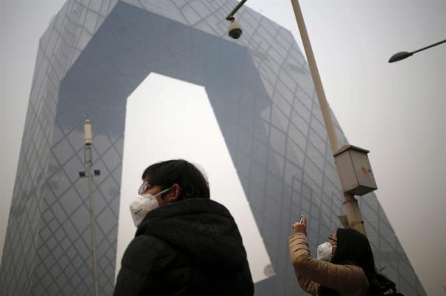 Dos viandantes con mascarillas permanecen ante China Central Television (CCTV) Tower en medio de la niebla en Pekín (China) hoy, miércoles 19 de noviembre de 2014. La Organización Mundial de la Salud (OMS) apremió hoy a los legisladores de Pekín a ultimar la ley para reforzar la prohibición del tabaco en los espacios públicos de la capital china, una norma que entró en vigor cinco años atrás y cuya repercusión fue mínima entre los ciudadanos locales. EFE/How Hwee Young