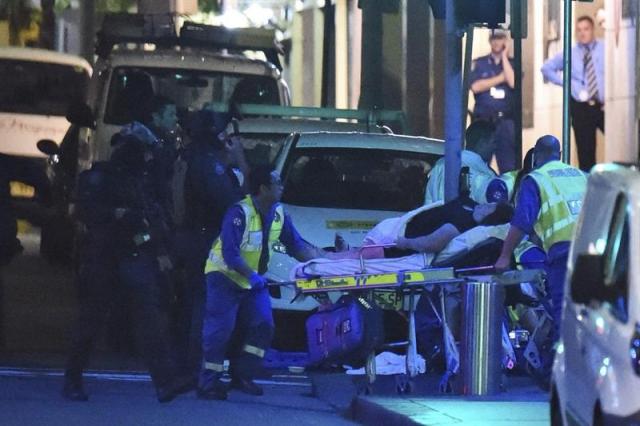 Miembros de los servicios médicos atienden a un herido junto a la cafetería tomada desde primeras horas de la mañana por un hombre armado en Sídney (Australia) hoy, lunes 15 de diciembre de 2014. La Policía de Australia ha declarado concluido el secuestro de personal y clientes de un café del centro de Sídney por un clérigo musulmán, después de que las fuerzas del orden irrumpieran en el local y liberaran a los rehenes. Al menos cuatro personas, incluidos rehenes, han resultado heridos en la operación policial. EFE/MICK TSIKAS 