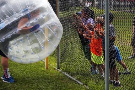 A "bubble soccer" participant talks to young kids through a chain link fence on Boston Common in Boston