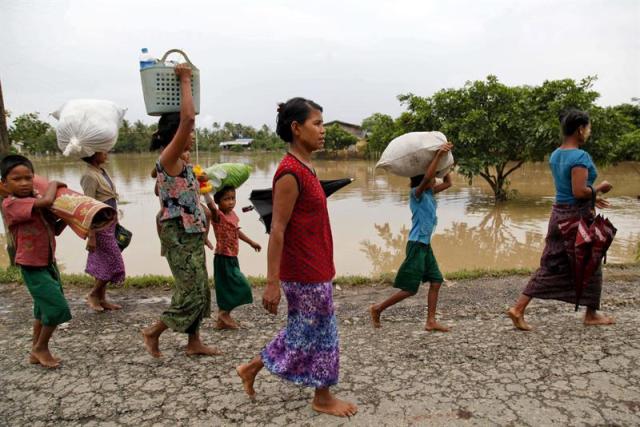 Varias persoans cargan con sus pertenencias tras evacuar sus calles en Min Pyar (Birmania) el pasado 2 de agosto de 2015. El Gobierno de Birmania (Myanmar) solicitó hoy ayuda internacional para asistir a los más de 210.000 damnificados por las inundaciones que azotan el país y admite su "débil" respuesta frente al desastre natural. Según los últimos datos oficiales, al menos 47 personas han perdido la vida, mientras Naciones Unidas alerta de un posible aumento "significativo" de víctimas y damnificados porque hay zonas aisladas a las que los equipos de rescate no han podido acceder. EFE/Nyunt Win