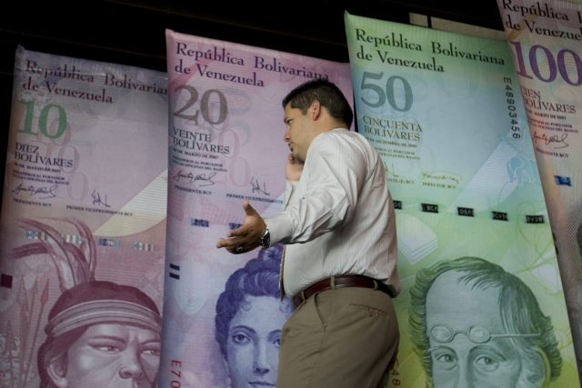 CAR01. CARACAS (VENEZUELA), 10/02/2015.- Un hombre habla por teléfono mientras camina frente a afiches de billetes venezolanos en la sede del Banco Centra de Venezuala (BCV) hoy, martes 10 de febrero de 2015, en la ciudad de Caracas (Venezuela). El vicepresidente para el Área Económica venezolano, Marcos Torres, anunció hoy que Venezuela creará a partir de mañana un sistema cambiario con tres modalidades y una de ellas será un mercado "totalmente libre" al que acudirán oferentes y demandantes de divisas tanto personas privadas como jurídicas. EFE/MIGUEL GUTIÉRREZ