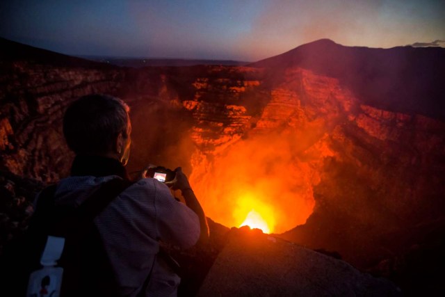 A tourist takes pictures of a lava lake inside the crater of the Masaya Volcano in Masaya, some 30km from Managua on May 19, 2016. Hundreds of tourists arrive daily to observe the lava flow which formed six months ago near the surface of the crater of the small Masaya volcano, one of the most active in Nicaragua. / AFP PHOTO / INTI OCON / TO GO WITH AFP STORY BY BLANCA MOREL