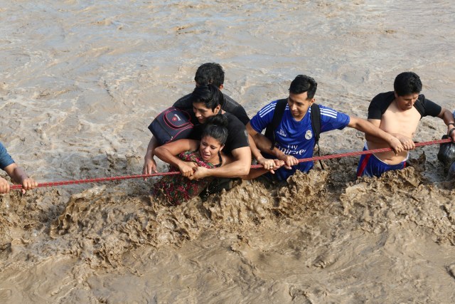 REFILE - CORRECTING NAME OF THE RIVER A woman is assisted while crossing a flooded street after the Huaycoloro river overflooded its banks sending torrents of mud and water rushing through the streets in Huachipa, Peru, March 17, 2017. REUTERS/Guadalupe Pardo