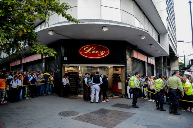 Forensic police stand next to the body of a man outside a supermarket, where he died of a heart attack after waiting in a long line to buy food, in Caracas on March 30, 2017. / AFP PHOTO / FEDERICO PARRA