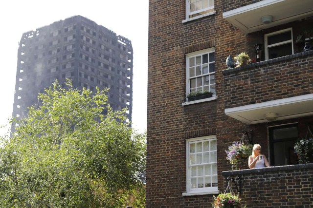 A local resident stands on her balcony by the gutted Grenfell Tower in west London on June 15, 2017. Firefighters searched for bodies today in a London tower block gutted by a blaze that has already left 12 dead, as questions grew over whether a recent refurbishment contributed to the fire. / AFP PHOTO / Tolga AKMEN