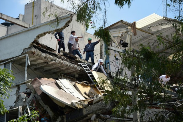 People stand at a building which collapsed after a quake rattled Mexico City on September 19, 2017. A powerful earthquake shook Mexico City on Tuesday, causing panic among the megalopolis' 20 million inhabitants on the 32nd anniversary of a devastating 1985 quake. The US Geological Survey put the quake's magnitude at 7.1 while Mexico's Seismological Institute said it measured 6.8 on its scale. The institute said the quake's epicenter was seven kilometers west of Chiautla de Tapia, in the neighboring state of Puebla. / AFP PHOTO / Ronaldo SCHEMIDT