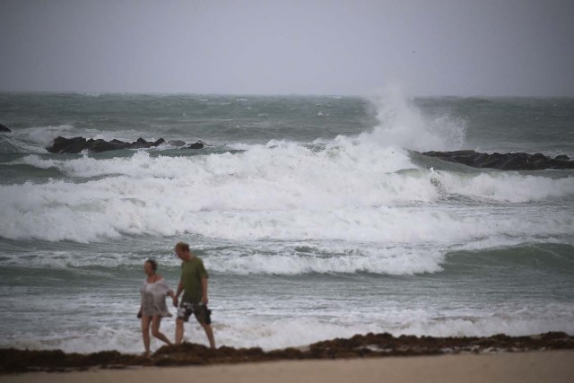 MIAMI BEACH, FL - SEPTEMBER 09: People walk along the beach storm as a churning ocean is seen behind them as Hurricane Irma approaches on September 9, 2017 in Miami Beach, Florida. Florida is in the path of the Hurricane which may come ashore at category 4.   Joe Raedle/Getty Images/AFP