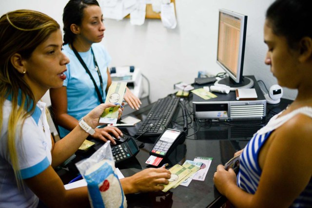 A cashier in the BanPanal communal bank explains the exchange value of the new local community currency, the panal, launched in the "23 de Enero" working-class neighbourhood in Caracas on December 15, 2017. A collective in a hilltop shantytown in Caracas created its own currency, the panal, in an attempt to fight chronic shortages of cash in inflation-ridden Venezuela. The currency can be exchanged locally for staples like sugar, rice (produced in the neighborhood itself), and bread. / AFP PHOTO / FEDERICO PARRA