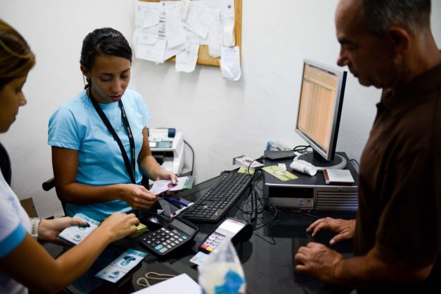 A cashier in the BanPanal communal bank explains the exchange value of the new local community currency, the panal, launched in the "23 de Enero" working-class neighbourhood in Caracas on December 15, 2017. A collective in a hilltop shantytown in Caracas created its own currency, the panal, in an attempt to fight chronic shortages of cash in inflation-ridden Venezuela. The currency can be exchanged locally for staples like sugar, rice (produced in the neighborhood itself), and bread. / AFP PHOTO / FEDERICO PARRA