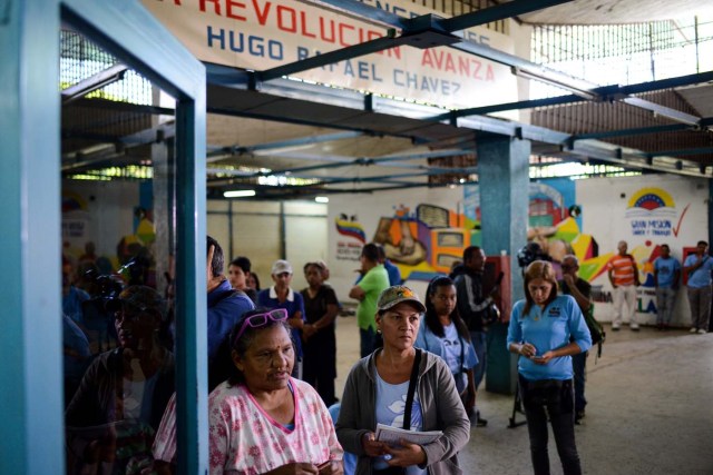 People queue outside the BanPanal communal bank to exchange bolivares for the new local community currency, the panal, launched in the "23 de Enero" working-class neighbourhood in Caracas on December 15, 2017. A collective in a hilltop shantytown in Caracas created its own currency, the panal, in an attempt to fight chronic shortages of cash in inflation-ridden Venezuela. The currency can be exchanged locally for staples like sugar, rice (produced in the neighborhood itself), and bread. / AFP PHOTO / FEDERICO PARRA