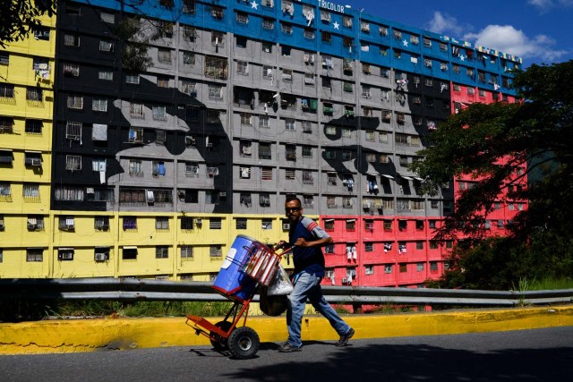 A man pushes a cart in the street past a building depicting the eyes of late Venezuelan president Hugo Chavez in the "23 de Enero" neighbourhood in Caracas on December 15, 2017. A collective in a hilltop shantytown in Caracas created its own currency, the panal, in an attempt to fight chronic shortages of cash in inflation-ridden Venezuela. The currency can be exchanged locally for staples like sugar, rice (produced in the neighborhood itself), and bread. / AFP PHOTO / FEDERICO PARRA