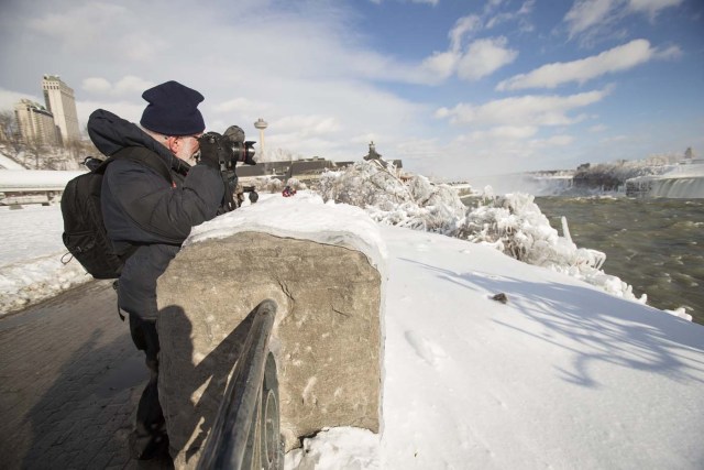 A tourist takes photos of the Horseshoe Falls in Niagara Falls, Ontario on January 3, 2018. The cold snap which has gripped much of Canada and the United States has nearly frozen over the American side of the falls. / AFP PHOTO / Geoff Robins