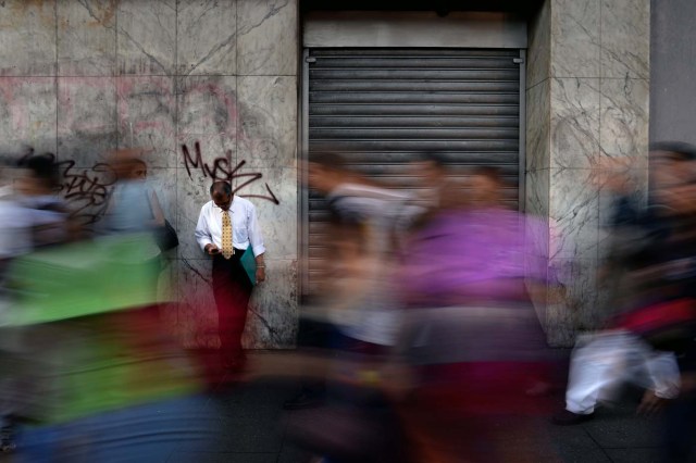 A man leans on a wall as people walk along a street during a partial power cut in Caracas on February 6, 2018. / AFP PHOTO / FEDERICO PARRA