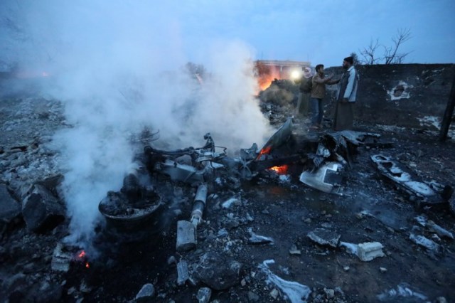 A picture taken on February 3, 2018, shows a Syrian men standing at the site of a downed Sukhoi-25 fighter jet near the Syrian city of Saraqib, southwest of Aleppo. Rebel fighters shot down a Russian plane over Syria's northwest Idlib province and captured its pilot, the Syrian Observatory for Human Rights said. / AFP PHOTO / OMAR HAJ KADOUR