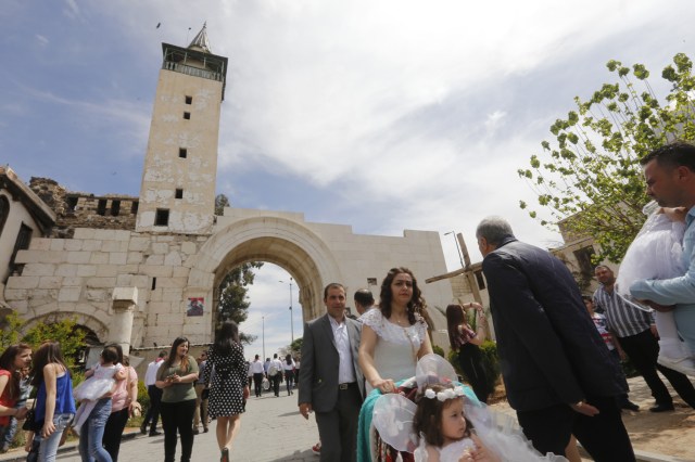 Syrian people walk down a street during a parade celebrating Easter in the Christian neighbourhood of Bab Sharqi in Old Damascus on April 1, 2018. / AFP PHOTO / Louai Beshara