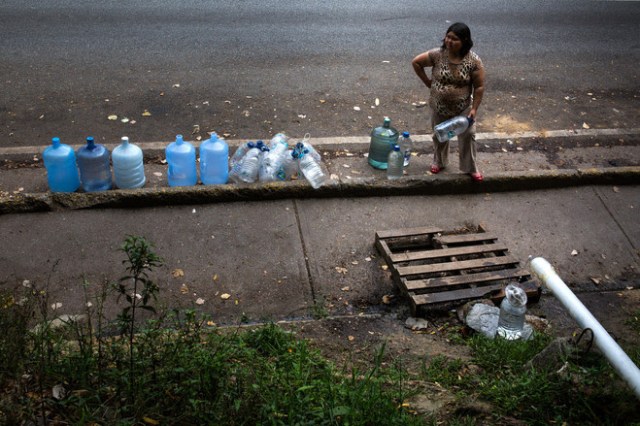 Una mujer llena botellas con el agua que gotea de un chorro resorte al lado de la Cota Mil en Caracas. FOTO: WIL RIERA PARA THE WALL STREET JOURNAL